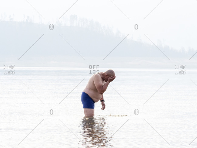 Senior man standing thigh deep in water, washing his face. Heat and smoke haze in the air from bush fires.