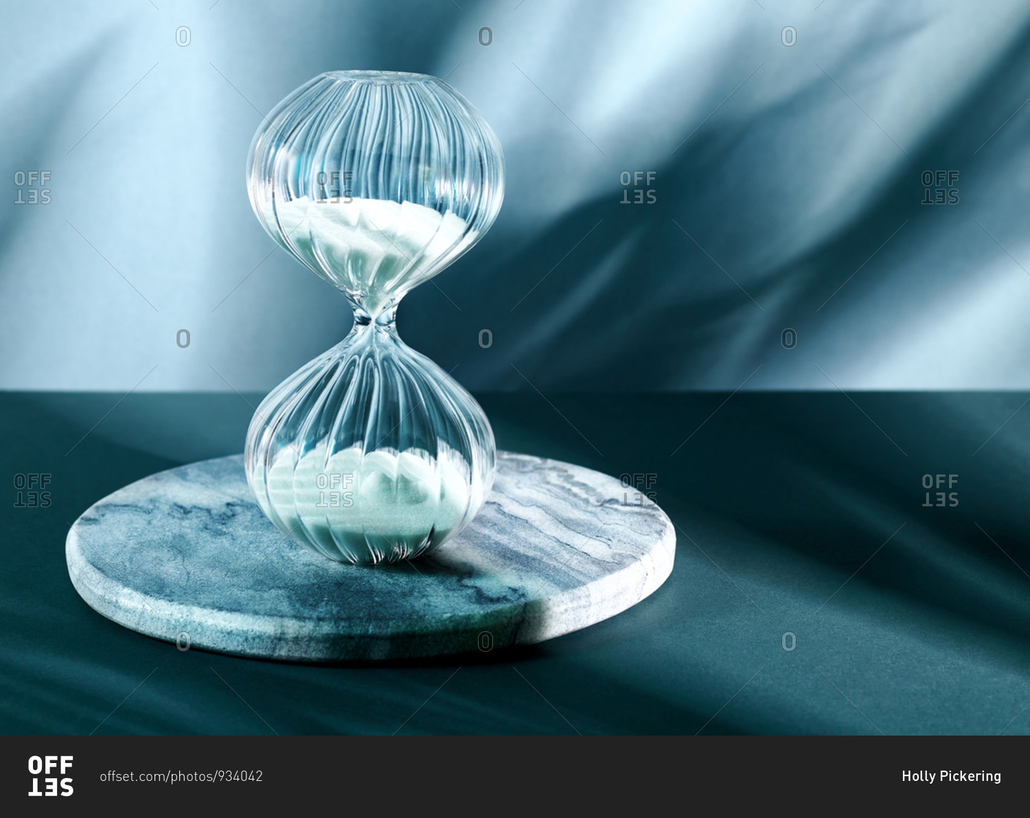 A decorative glass hourglass sand timer against a shadowy blue background