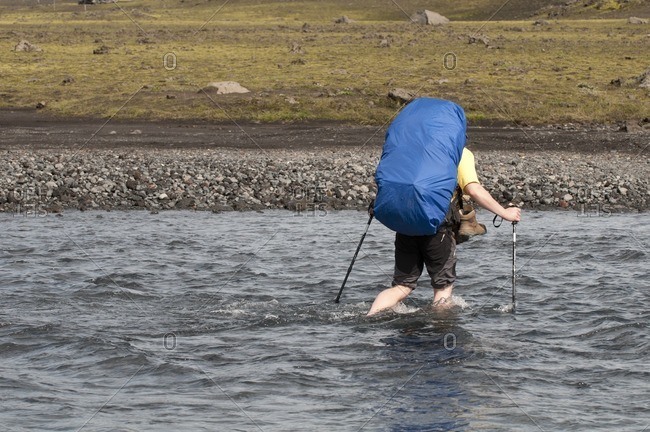Hiker crosses a river on the way from Skogar to Landmannalaugar, Iceland, Europe