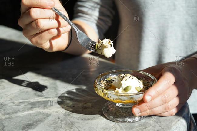 Young woman holding a scoop of yoghurt, seeds and honey sunlight..
