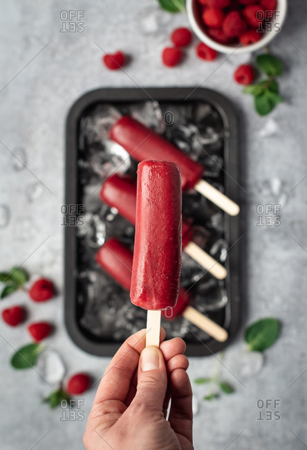 Hand holding raspberry popsicle above a tray of frozen treats.