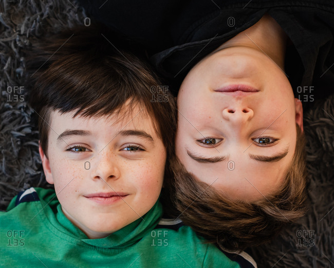 Looking down at the faces of two boys laying beside each other.