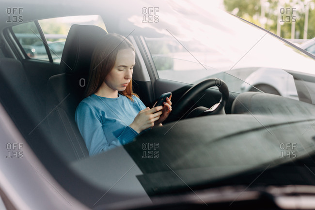 Serious woman holding her smart phone while sitting inside the car.