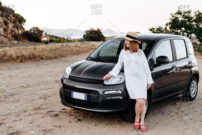 Cute, charming girl in a straw hat poses around a black car on the roadside  Stock Photo - Alamy