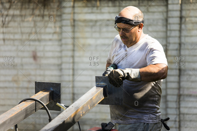 Metal worker fabricating metal posts in outdoor workshop.