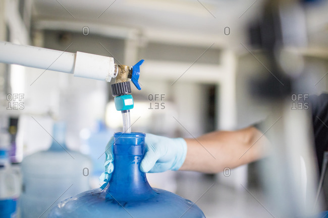 Worker holds top of water jug while filling it with drinking water.