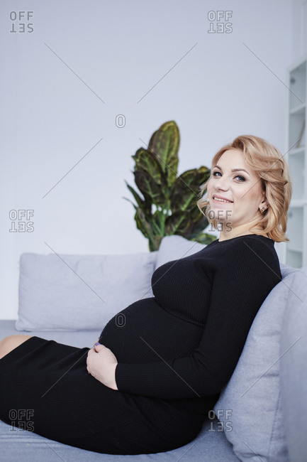 Pregnant woman in black dress touching tummy and smiling