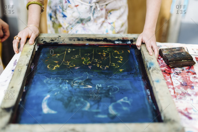 Crop woman placing silkscreen on textile before pouring ink