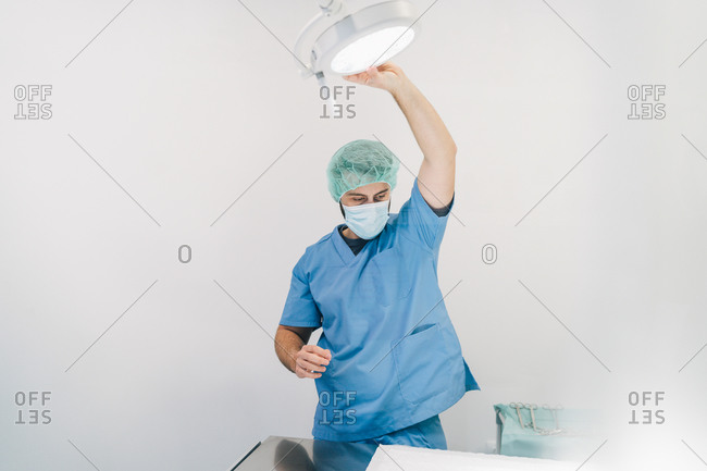 Man in blue medical uniform with a mask and hygienic cap preparing the light on the operating table in a veterinary clinic