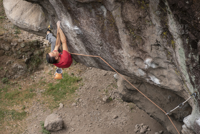 One man wearing red holds with both hands on rock wall while climbing