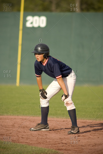 young baseball player on base path with his hands on his knees
