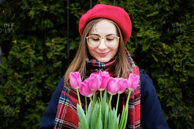 Young French millennial girl in beret and coat with tulips in hands