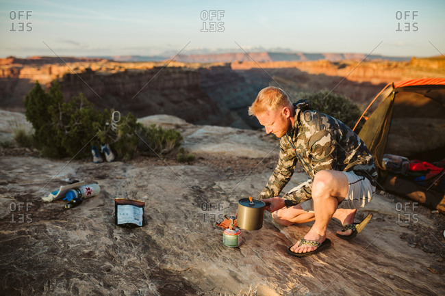 Male camper boils water with a whisper light at camp in desert