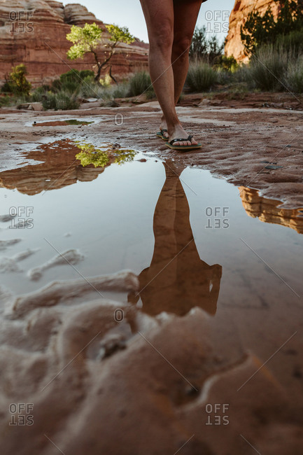 Reflection in puddle of woman's legs walking in flipflops in desert mu