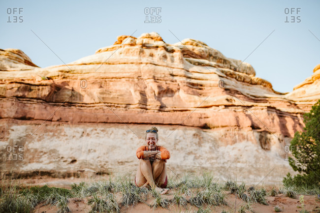 Blonde woman sits cross-legged and laughs in the desert of Utah