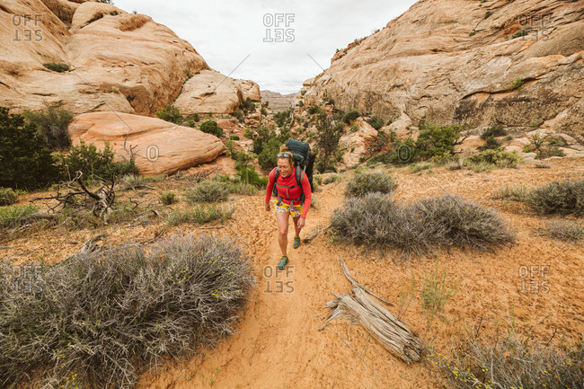 Woman backpacks through sand under sandstone canyons of canyonlands