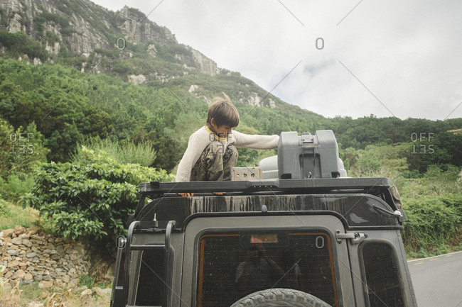 A kid sits on top of a four wheel drive car in the countryside