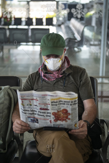 Khajuraho, MP, India - March 16, 2020: Middle aged man reads about Covid-19 while waiting at a deserted airport in Khajuraho, Madhya Pradesh, India, wearing a face mask to stay protected.