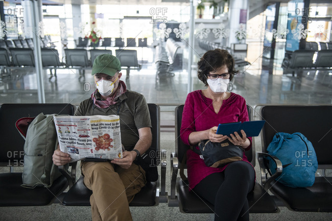 Khajuraho, MP, India - March 16, 2020: Middle aged couple wear face masks due to the Coronavirus pandemic while waiting at a deserted airport in Khajuraho, Madhya Pradesh, India.