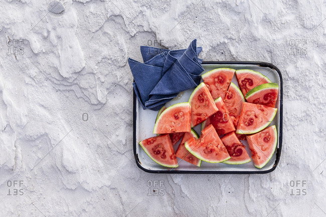 Slices of watermelon on tray on textured sandy background