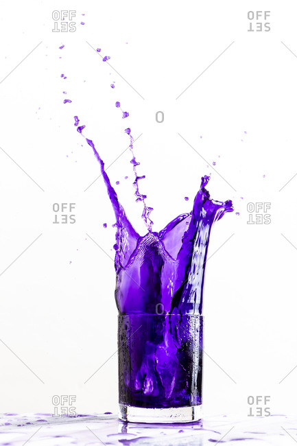 Ice dropped into a glass of vibrant purple beverage creates a dynamic splash against a white background