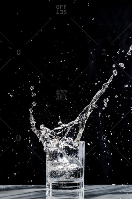 Ice creates a splash in a glass of sparkling water in a cocktail glass  against a black background stock photo - OFFSET