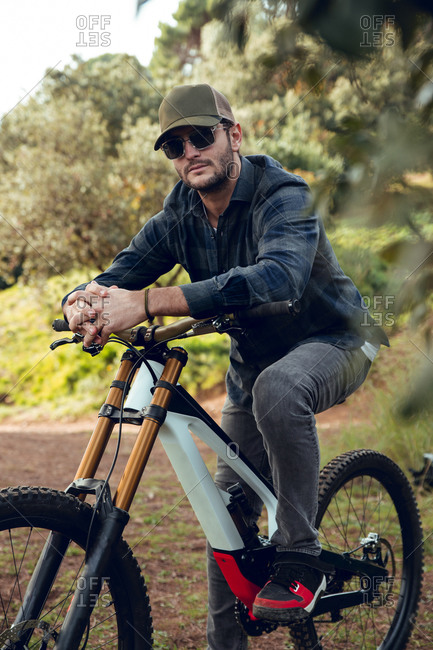 Mountain biking sportsman without protection sitting on bike in the middle of a forest looking at camera
