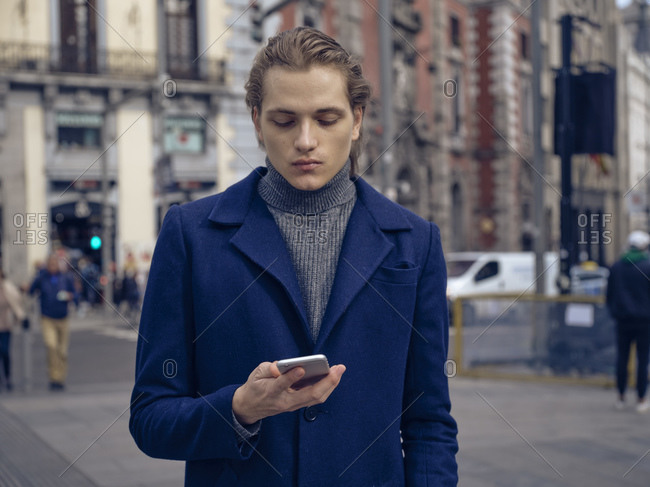 Stylish young man browsing on smartphone on street on city street