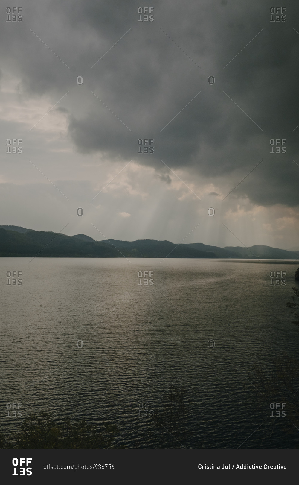Tranquil landscape with sun rays shining through thick clouds over calm lake with dark water
