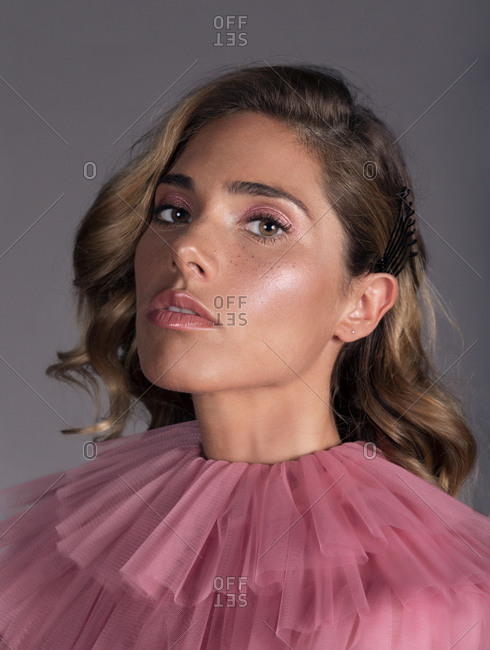 Portrait of pretty young blonde woman in a pink dress looking at camera while sitting against grey background