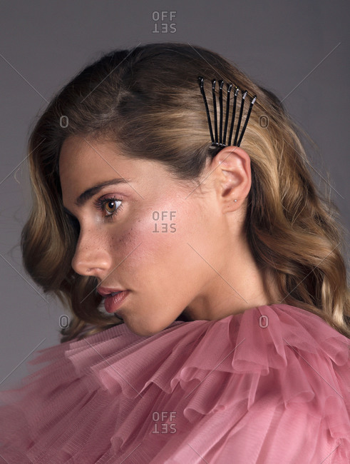 Side view portrait of pretty young blonde woman in a pink dress looking away while sitting against grey background