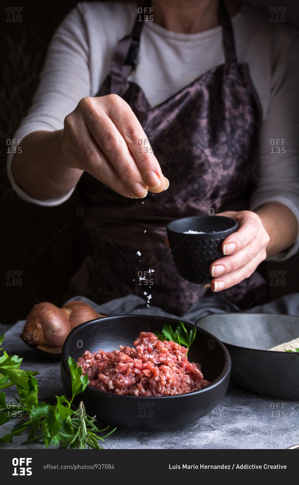 Anonymous female in apron spilling salt on fresh minced meat while preparing lunch in kitchen