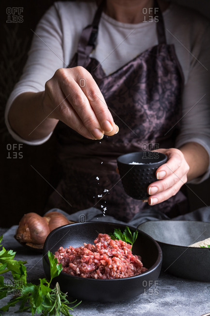 Anonymous female in apron spilling salt on fresh minced meat while preparing lunch in kitchen