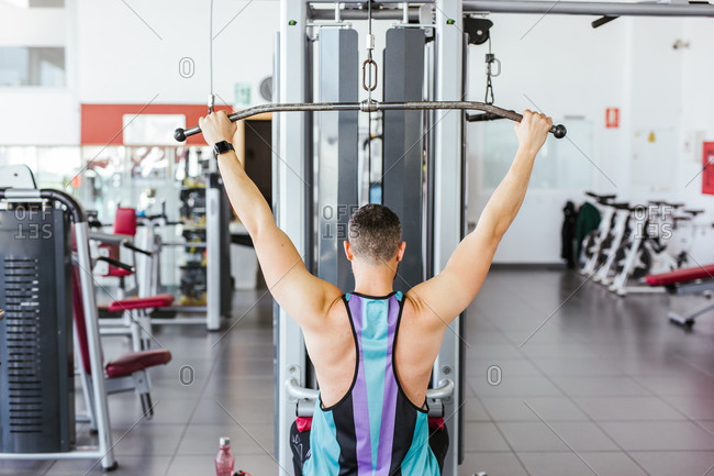 From above back view of unrecognizable sportsman in sports clothes performing exercise on weight machine against blurred interior of contemporary sport club
