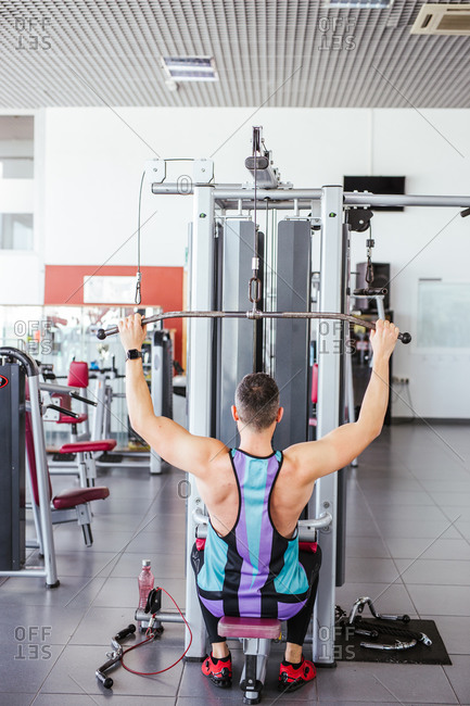 From above back view of unrecognizable sportsman in sports clothes performing exercise on weight machine against blurred interior of contemporary sport club