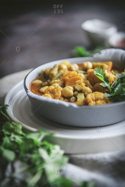 Bowl with tasty chickpea curry and herbs placed near gray cloth napkin in rustic setting