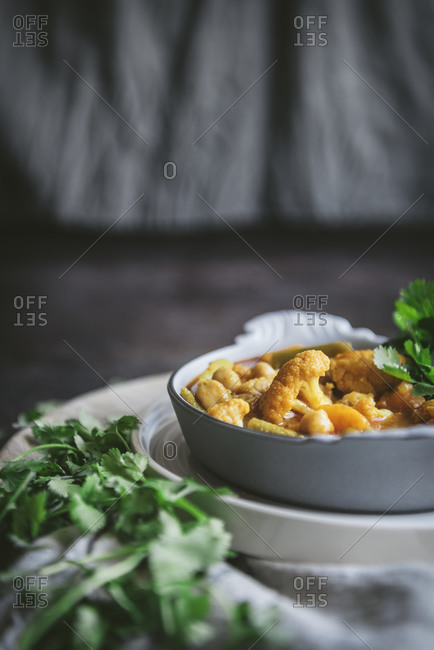Bowl with tasty chickpea curry and herbs placed near gray cloth napkin in rustic setting