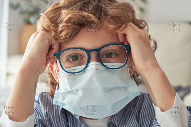 Smart boy in medical mask and glasses looking at camera while spending time at home during quarantine