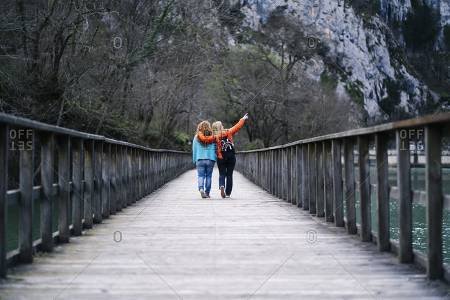 Back view of two best friends walking side by side on boardwalk- Valdemurio Reservoir- Asturias- Spain