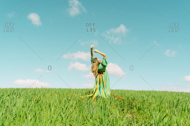 Young woman wearing a green dress bending over backwards in a field
