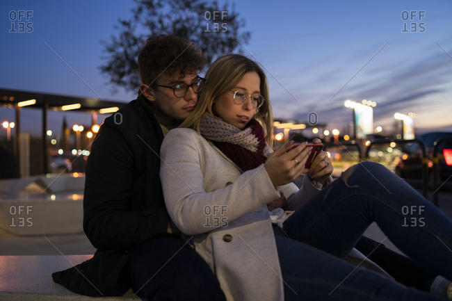 Young couple using smartphone at evening twilight