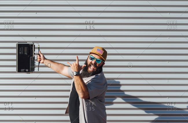 Portrait of bearded man with portable radio screaming and showing Rock And Roll Sign
