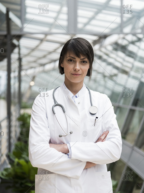 Portrait of female doctor with stethoscope- standing in atrium- with arms crossed