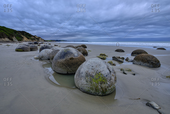 New Zealand- Otago- Moeraki- Clouds over cluster of Moeraki Boulders lying on Koekohe Beach at dusk