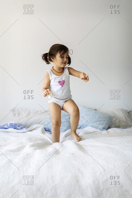 Portrait of little girl in underwear dancing on bed stock photo - OFFSET