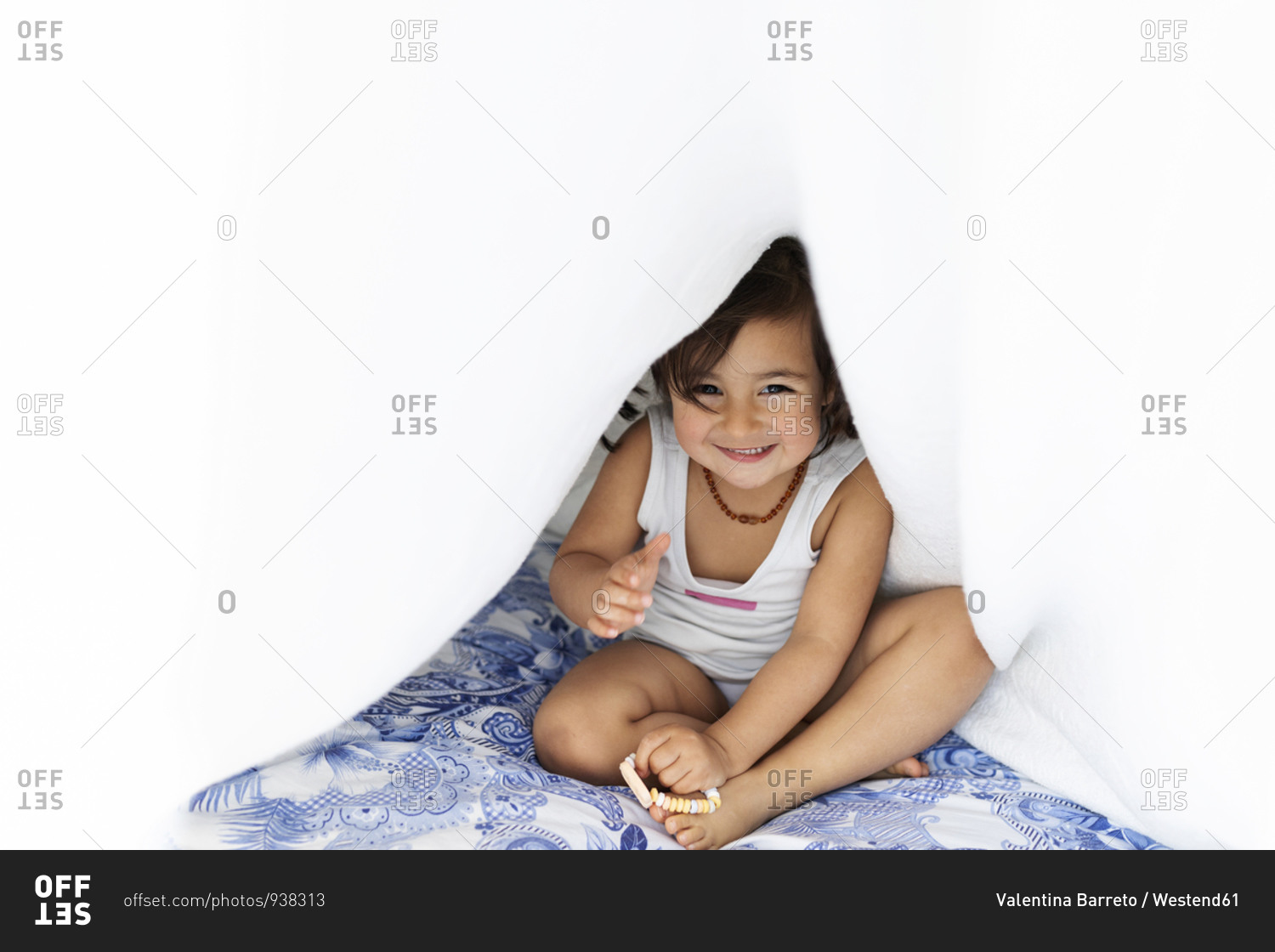 Portrait of little girl sitting on bed hiding under blanket stock photo
