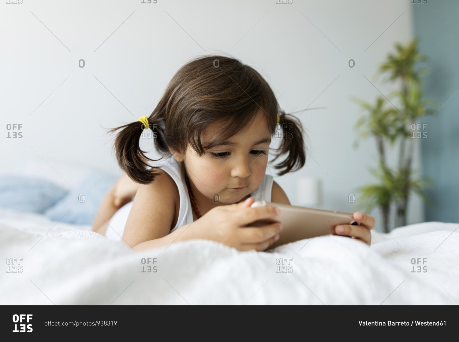 Little girl in underwear sitting on bed looking at smartphone stock photo -  OFFSET