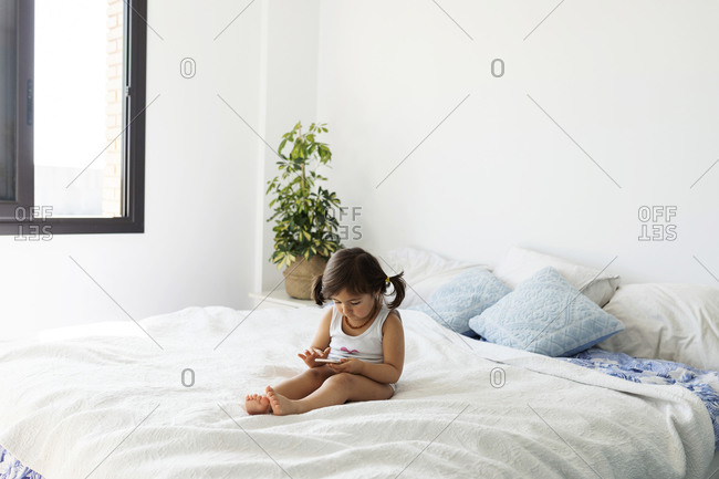 Little girl in underwear sitting on bed using smartphone stock