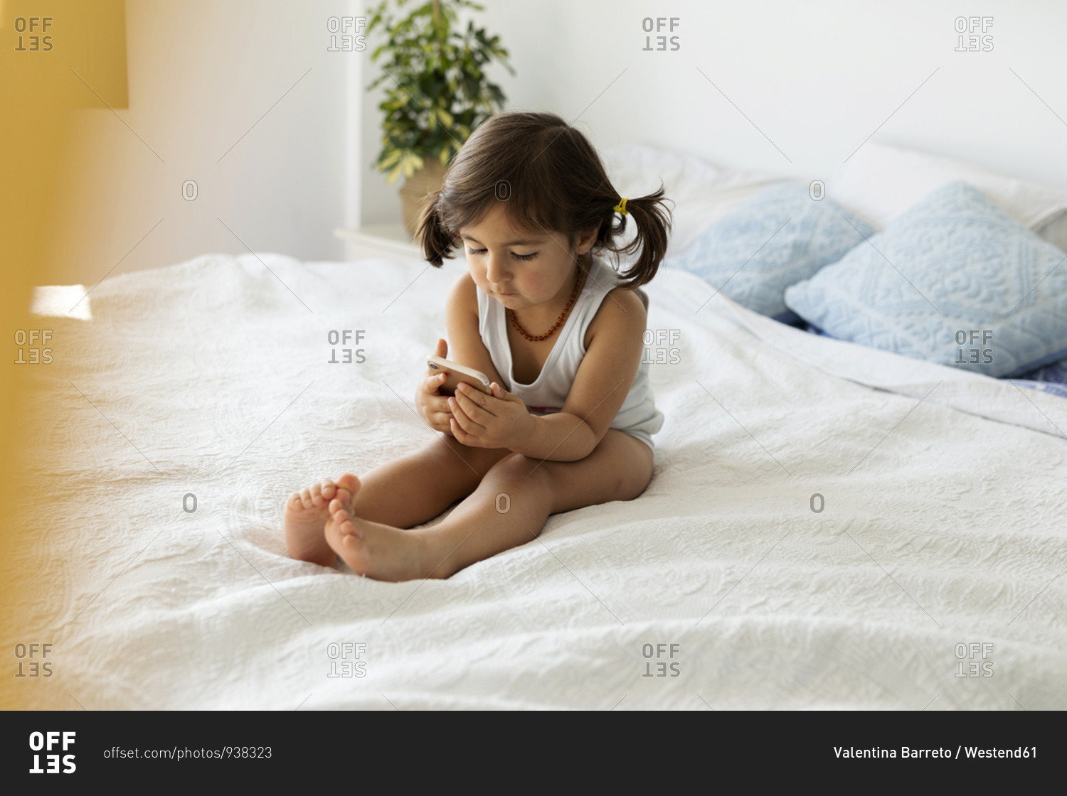 Little girl in underwear sitting on bed looking at smartphone
