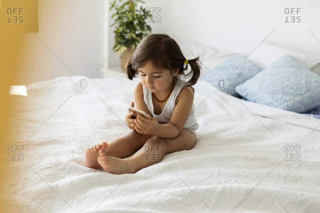 Little girl in underwear sitting on bed looking at smartphone stock photo -  OFFSET